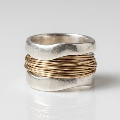 Anillo artesanal de plata y oro con bandas entrelazadas, creado por la marca Rose & Oliver, mostrado sobre un fondo neutro