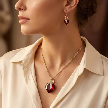 Conjunto de joyas Rose & Oliver con corazón torcido en oro y rubíes, que incluye aretes y collar delicado con piedras rojas.