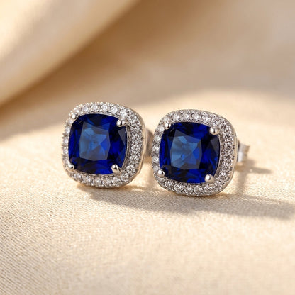 Brincos de prata com safira em halo, estilo stud, da marca Rose & Oliver, com design elegante e brilhante.