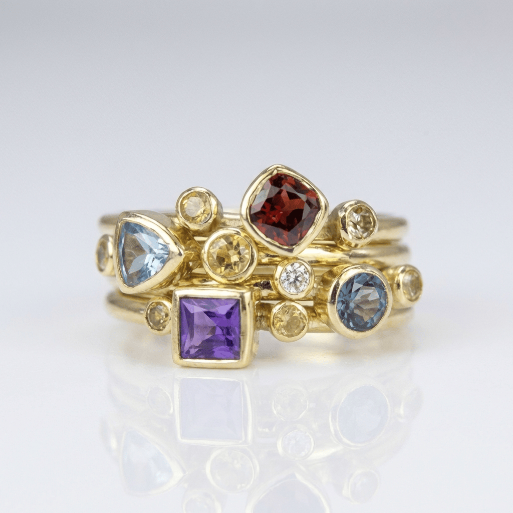 Conjunto de anillos apilados con piedras preciosas coloridas en oro, joyas de la marca Rose & Oliver, muestra detalles vibrantes y elegantes.